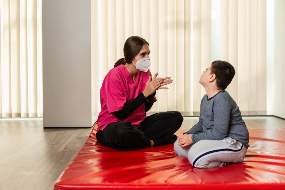 disabled child and physiotherapist on a red gymnastic mat