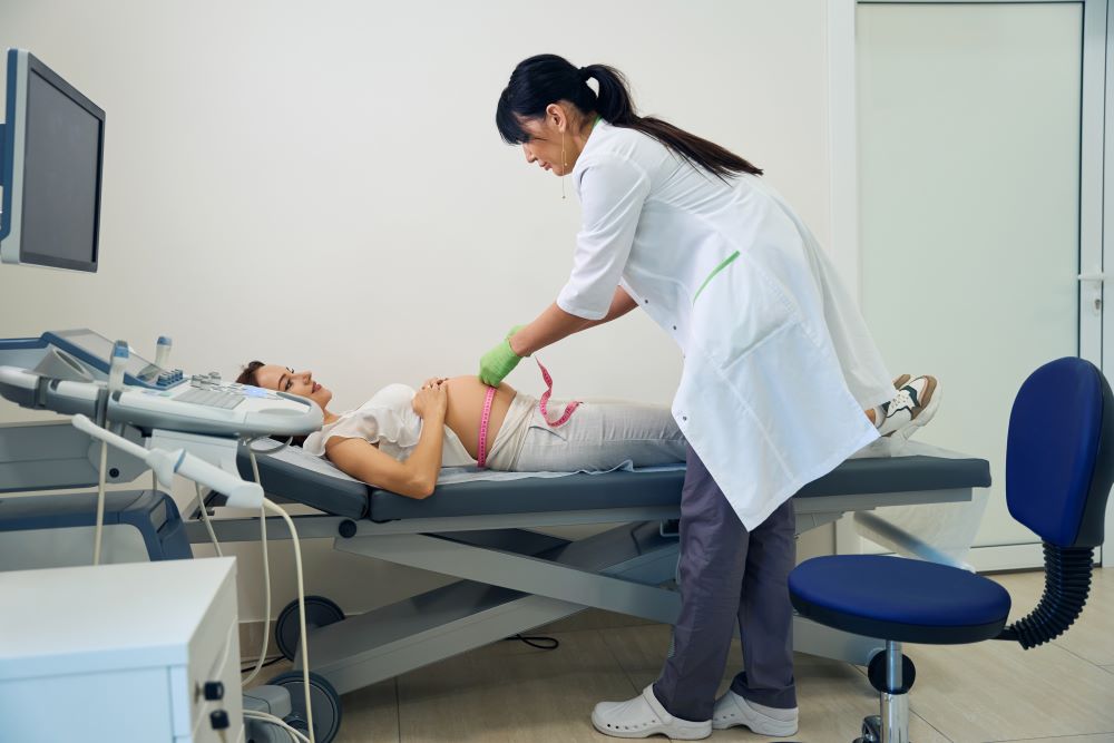 Side view of female gynecologist measuring belly with tape of pregnant woman