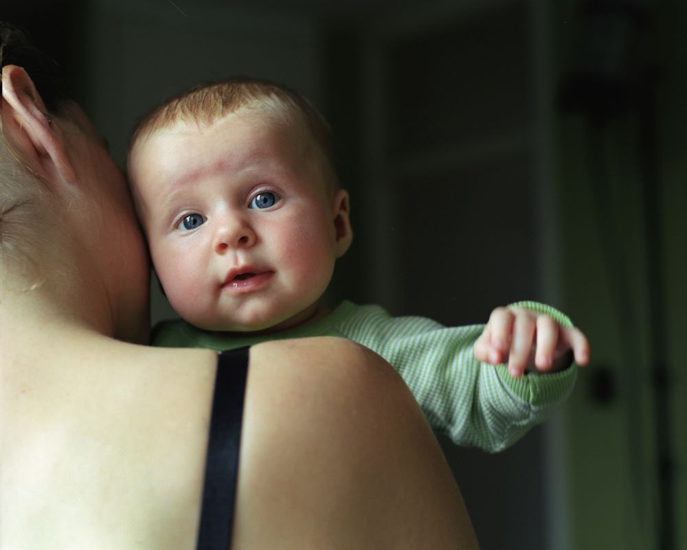 Close-up of a baby gazing over their mother’s shoulder